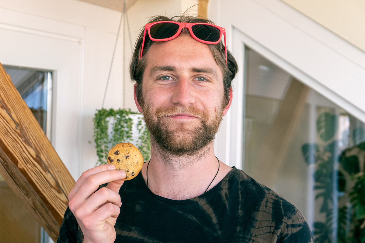 Photo portrait de Pierre avec des lunettes de soleil orange et tenant un biscuit dans sa main droite