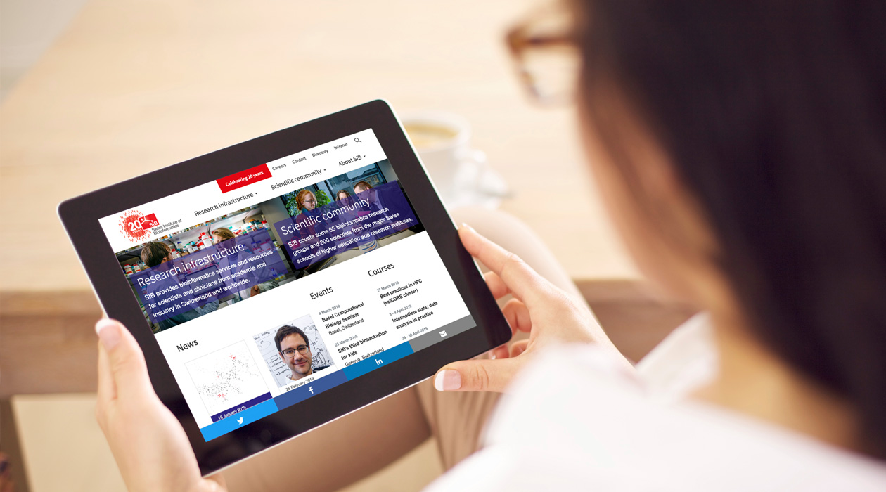 Femme avec des lunettes qui tient entre ses mains une tablette en regardant la page d'accueil du Swiss Institute of Bioinformatics
